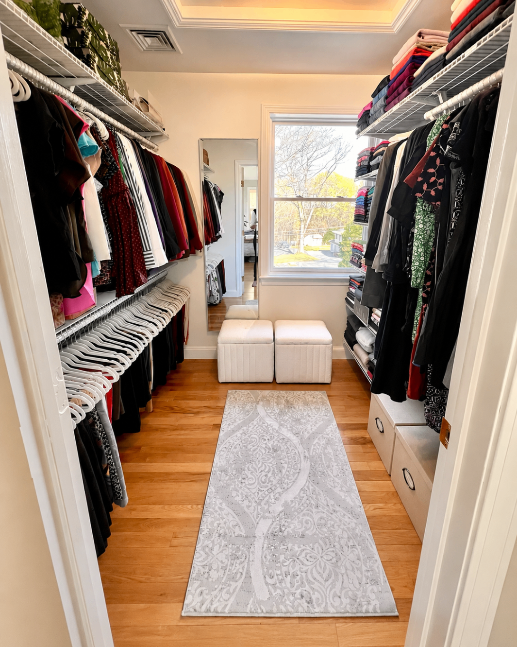 Narrow closet with a window, light rug, and clothing organized along the sides.